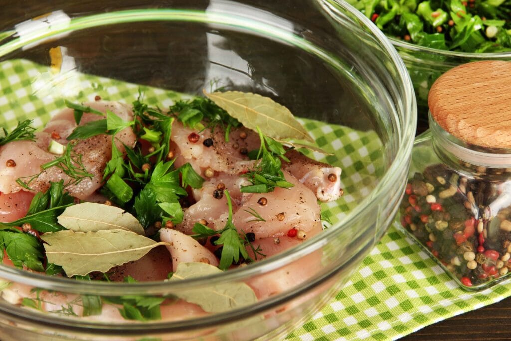 Turkey breast submerged in a brine solution with herbs and spices in a glass bowl
