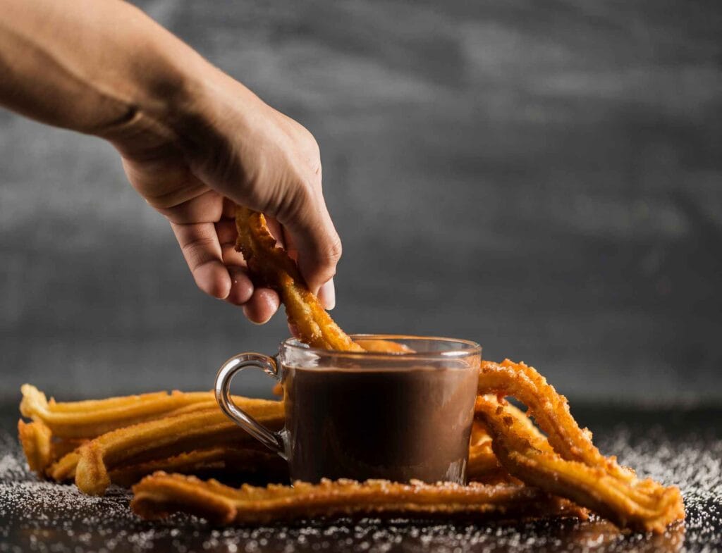 Churros being dipped into a pot of hot chocolate at a festive market.