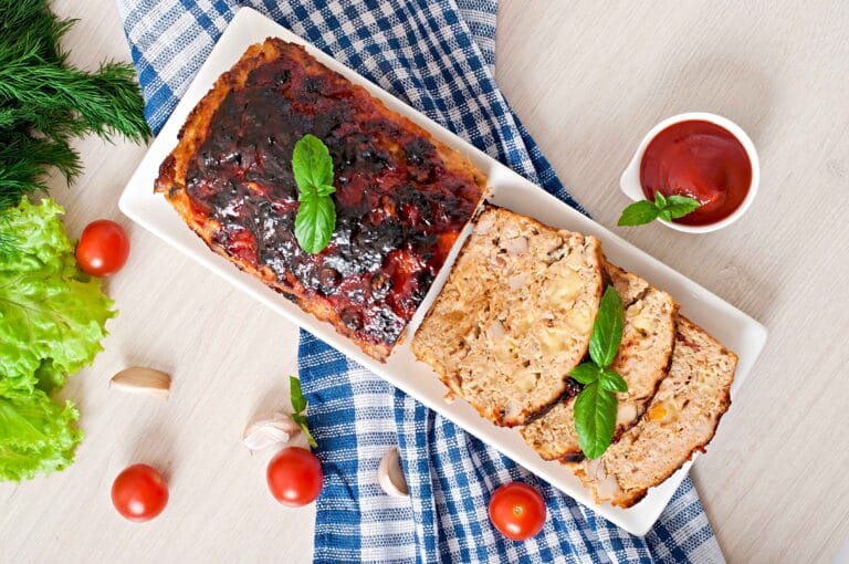 A freshly baked meatloaf with a shiny glaze on top, sliced to reveal a moist interior.