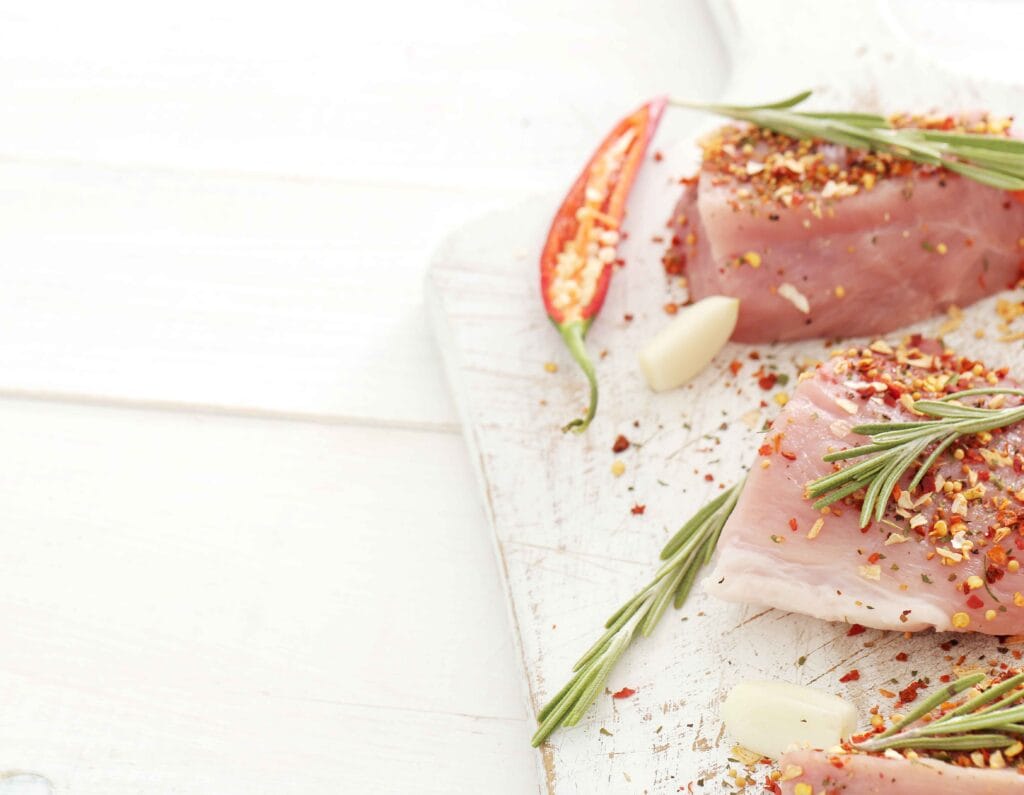 Raw turkey breast being seasoned with herbs and spices.