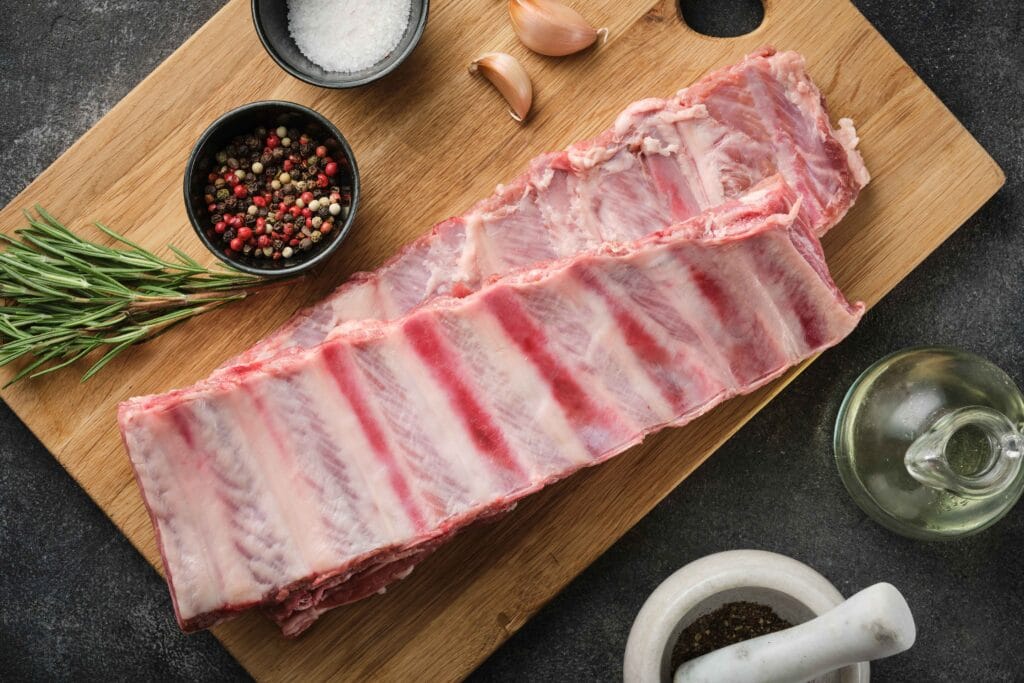 Raw beef back ribs on a cutting board with spices and herbs