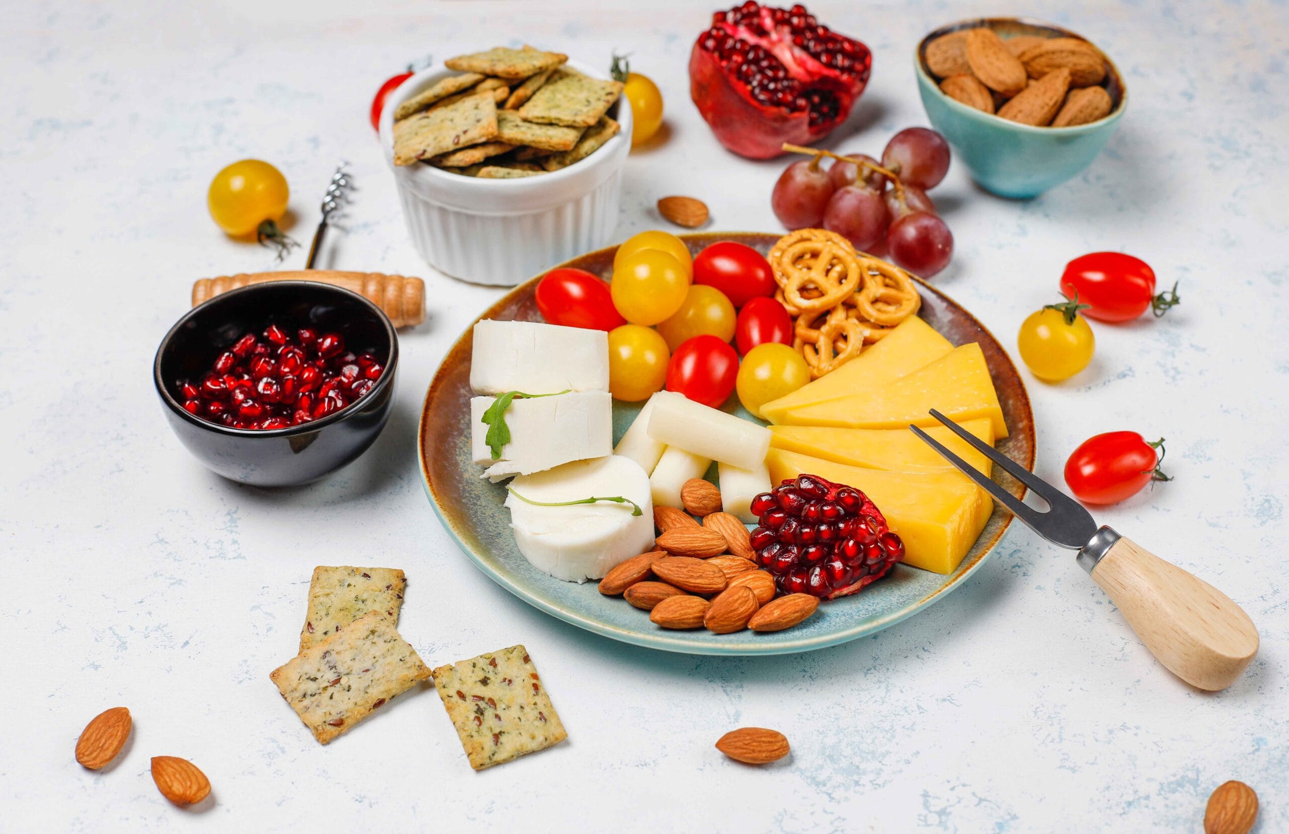 A bowl of cottage cheese surrounded by fresh fruits, vegetables, nuts, and seasonings.