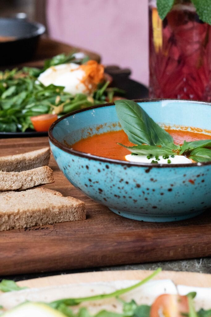 A loaf of crusty baguette next to a bowl of tomato soup.