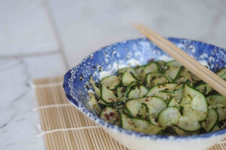 A vibrant bowl of cucumber kimchi with chili and garlic on a wooden table.