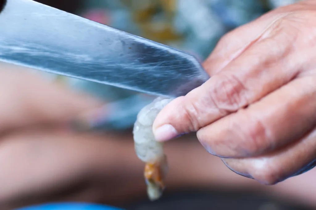 A person removing the vein from a raw shrimp using a paring knife