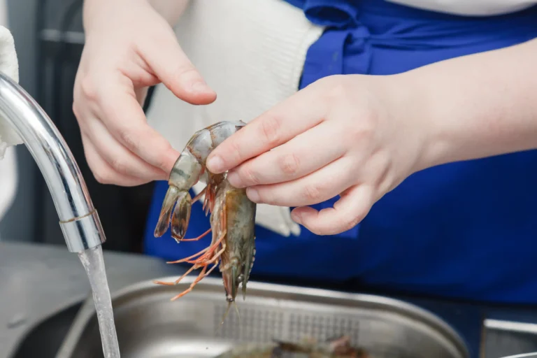 Raw shrimp being rinsed under cold water in a colander