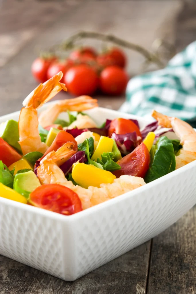 A mixed green salad, grilled vegetables, and a watermelon salad paired with BBQ shrimp.