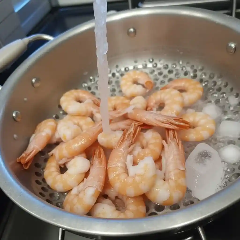 Thawed shrimp being rinsed in a kitchen sink with ice nearby